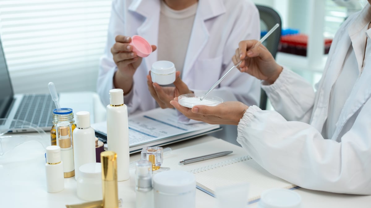 Dos especialistas en bata blanca revisando muestras de cosmética en un laboratorio luminoso